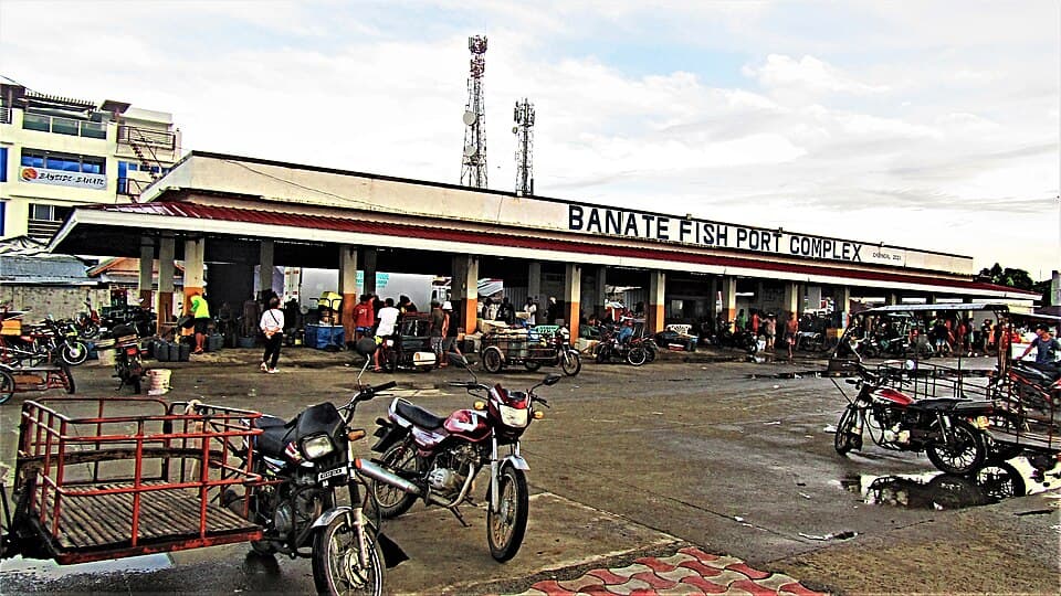 The Banate Fish Port Complex in Banate, Iloilo, a community fish landing building with a red roof and its name painted on the front, with motorcycles and tricycles parked outside