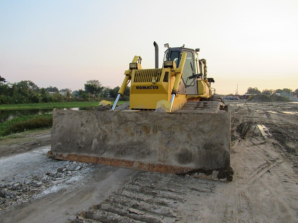 A yellow Komatsu bulldozer with its blade lowered on a dirt road construction site in Santo Tomas, Pampanga, at dusk