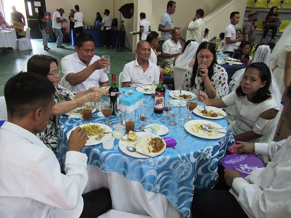 Newlywed couples and guests eating at a reception table after a Kasalang Bayan mass wedding in San Rafael, Bulacan, shown as a representative example of a Philippine mass wedding
