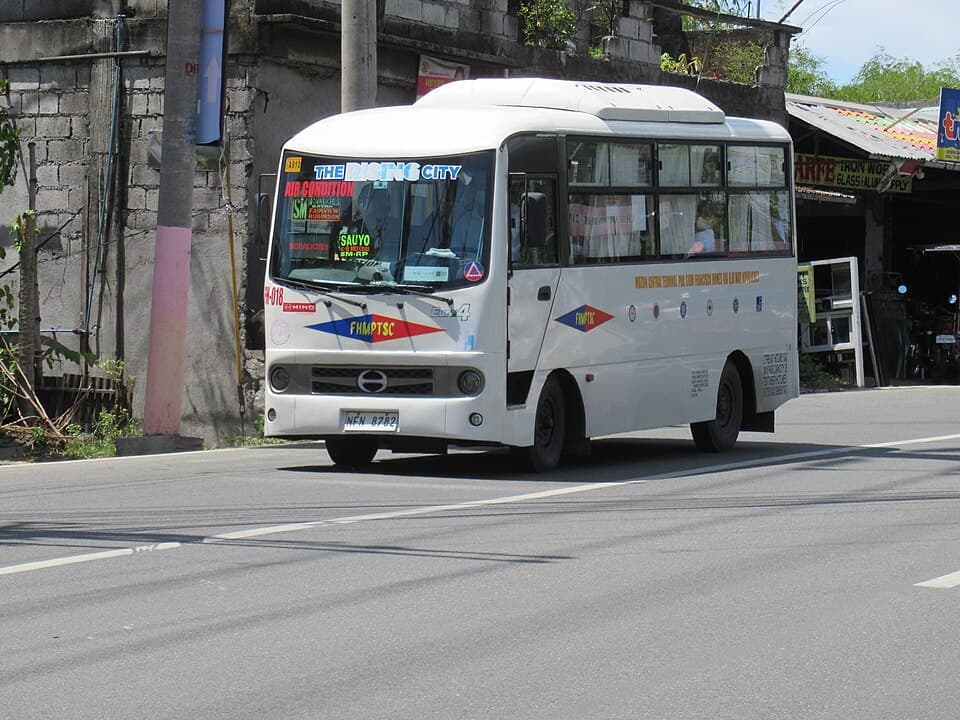 A white air-conditioned minibus run by the Francisco Homes Multi-Purpose Transport Service Cooperative on a road in San Jose del Monte, Bulacan