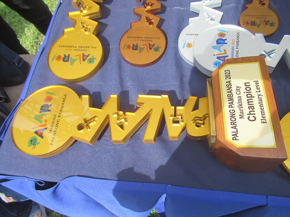 Gold, bronze and white Palarong Pambansa 2023 medals and a Marikina City elementary champion trophy laid on a table at the 2023 games