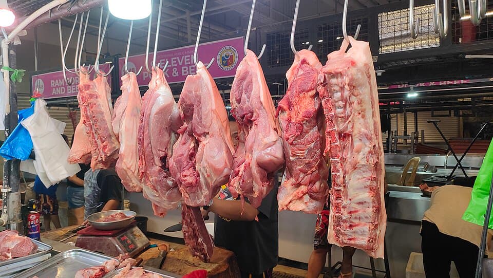Fresh pork slabs hanging from steel hooks at a meat vendor's stall inside the Iloilo Terminal Public Market in Iloilo City