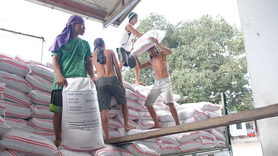 Workers unloading and stacking white sacks of rice at a rice warehouse in the Philippines
