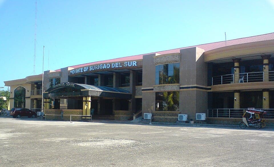 The two-storey Surigao del Sur Provincial Capitol building in Tandag City, with the words Province of Surigao del Sur on its facade and a tricycle parked in front
