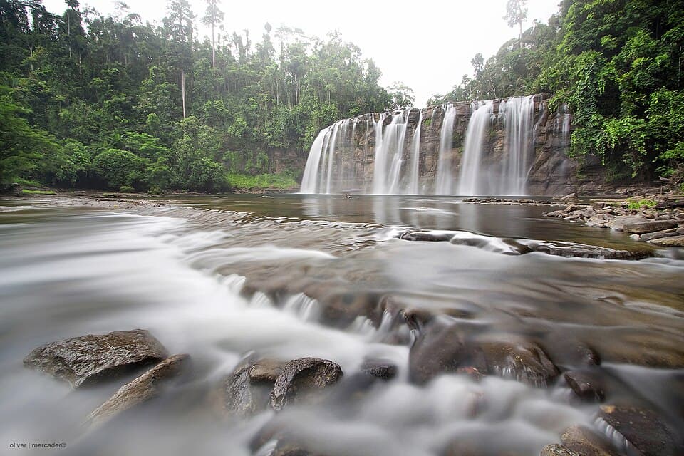 Long-exposure view of Tinuy-an Falls in Bislig, with water flowing over the wide rock face and across the boulders in the foreground