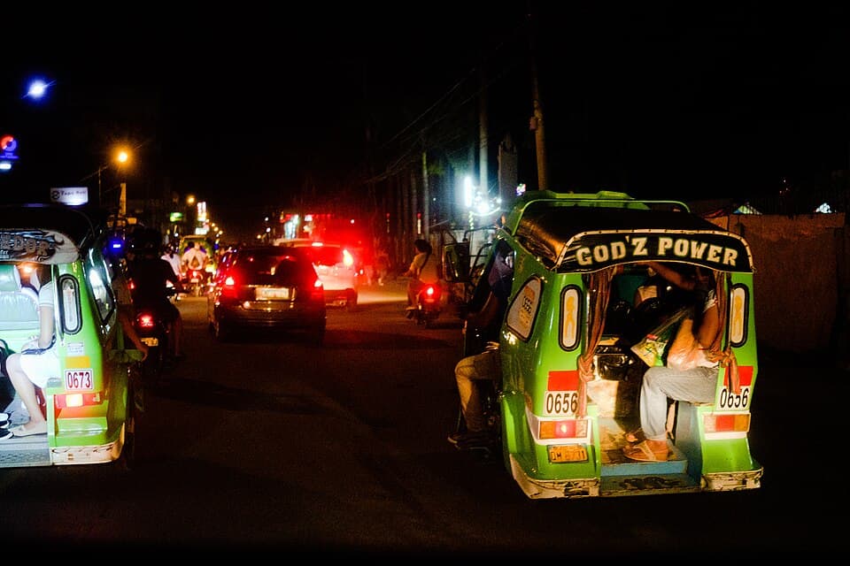 Green tricycles with numbered plates carrying passengers along a street at night outside Tagum City, Davao del Norte, shown as a representative example of Mindanao tricycles