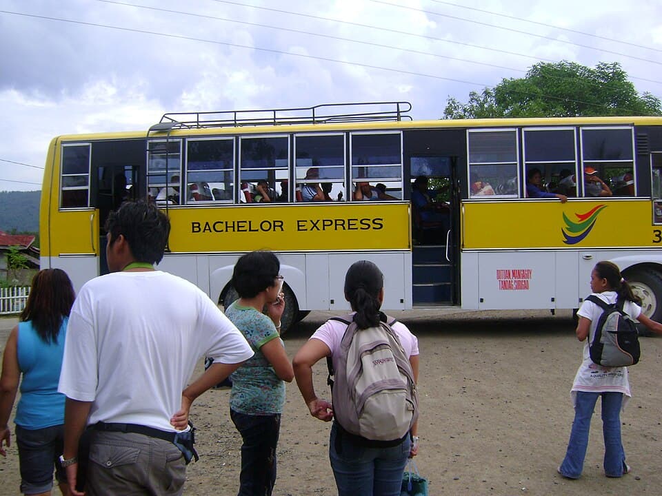 Passengers wait beside a yellow Bachelor Express bus with a Butuan, Mangagoy, Tandag and Surigao route sign, photographed in Bayabas, Surigao del Sur, in 2008