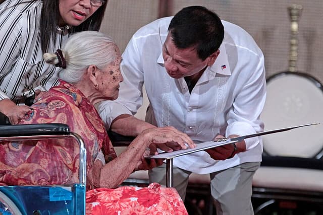 Former President Rodrigo Duterte shows the signed rules of the Centenarians Act of 2016 to 108-year-old Lourdes Marquez of Caloocan City at Malacañan in September 2016