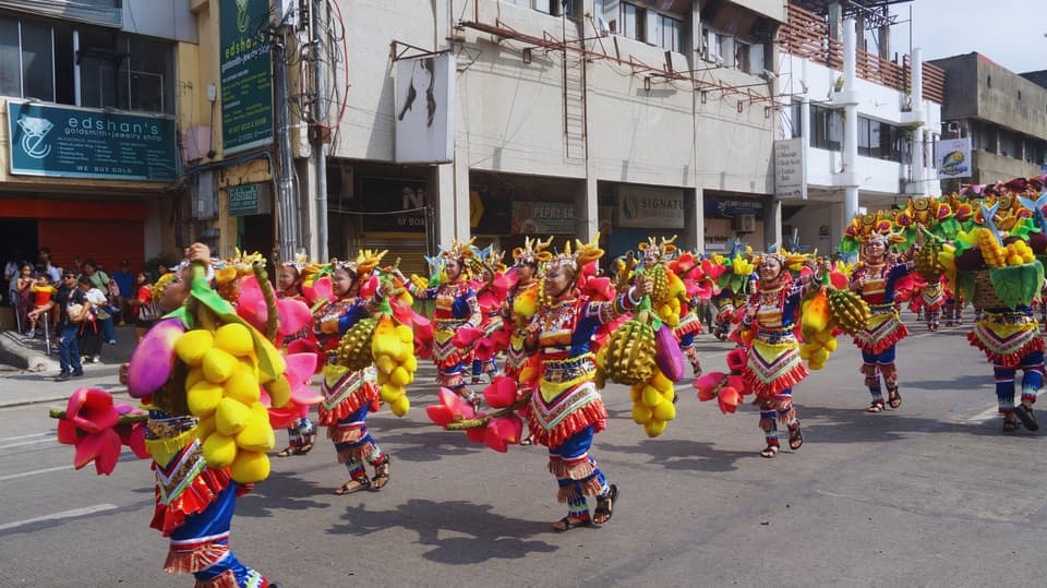 Dancers in colorful costumes carrying oversized fruit props, including durian and bananas, during the Indak-Indak sa Kadayawan 2026 street dance in Davao City (contingent not identified)