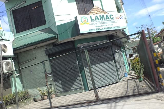 The Minglanilla branch office of LAMAC Multi-Purpose Cooperative in Cebu, a two-storey building with its sign above closed roll-up doors