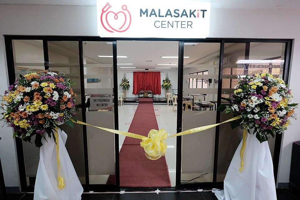 The glass entrance of a Malasakit Center with a lit sign above, a red carpet and a yellow ribbon between two flower arrangements, at its 2020 launch at the Davao Oriental Provincial Medical Center