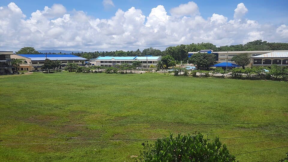 The open field of the North Eastern Mindanao State University main campus in Tandag City, with school buildings in the background, photographed from a rooftop