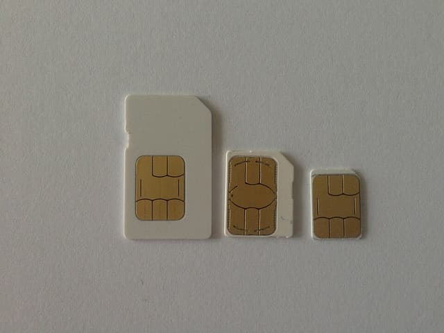 Three mobile phone SIM cards on a plain grey surface, showing the mini-SIM, micro-SIM and nano-SIM sizes from left to right