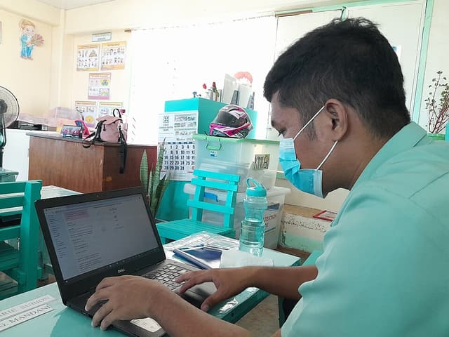 A teacher in a face mask works on a laptop inside a kindergarten classroom at Bislig Elementary School in 2022
