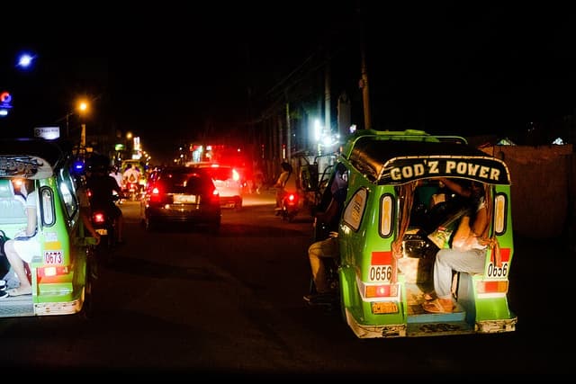 Green tricycles with numbered plates carrying passengers along a street at night outside Tagum City, Davao del Norte, shown as a representative example of Mindanao tricycles